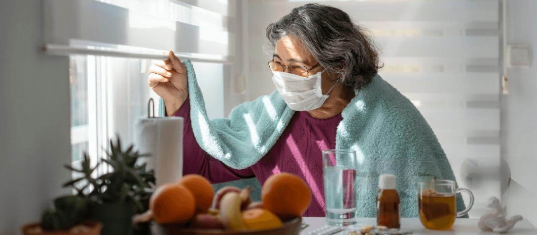 Femme avec un long COVID portant un masque, regardant par la fenêtre.