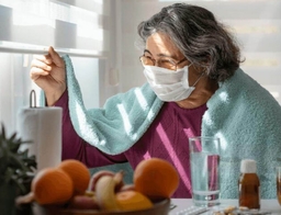 Femme avec un long COVID portant un masque, regardant par la fenêtre.