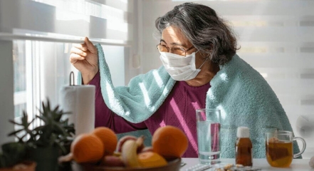 Femme avec un long COVID portant un masque, regardant par la fenêtre.