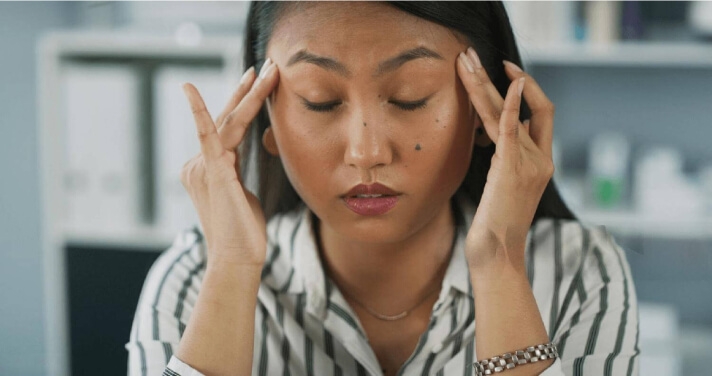 Femme présentant de longs symptômes de COVID, les yeux fermés, massant son front